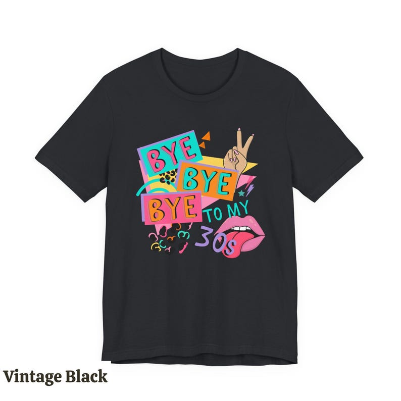 Puede incluir: Una camiseta negra de manga corta con un estampado gr&aacute;fico colorido que incluye el texto BYE BYE BYE TO MY 30s. El dise&ntilde;o muestra una mano haciendo el signo de la paz, labios rosas con la lengua fuera y varias formas geom&eacute;tricas brillantes.