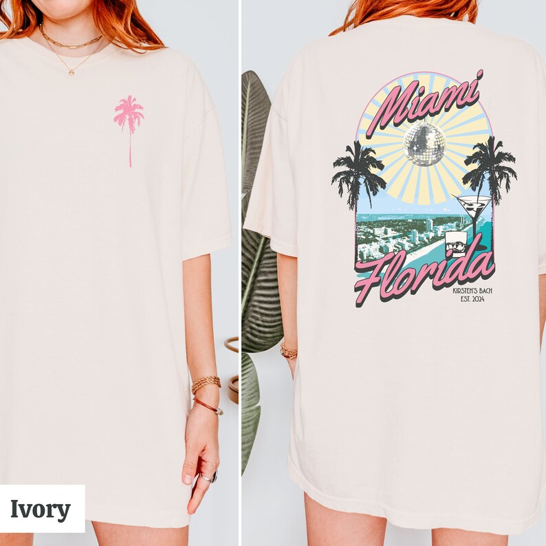 May include: Ivory oversized t-shirt with a pink palm tree graphic on the front and a graphic on the back that says "Miami Florida" with a palm tree, a disco ball, and a martini glass. The graphic also says "Kirstein's Bach Est. 2014".