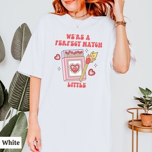 May include: White t-shirt with a graphic of a matchbox with a heart and the text "We're a perfect match little".