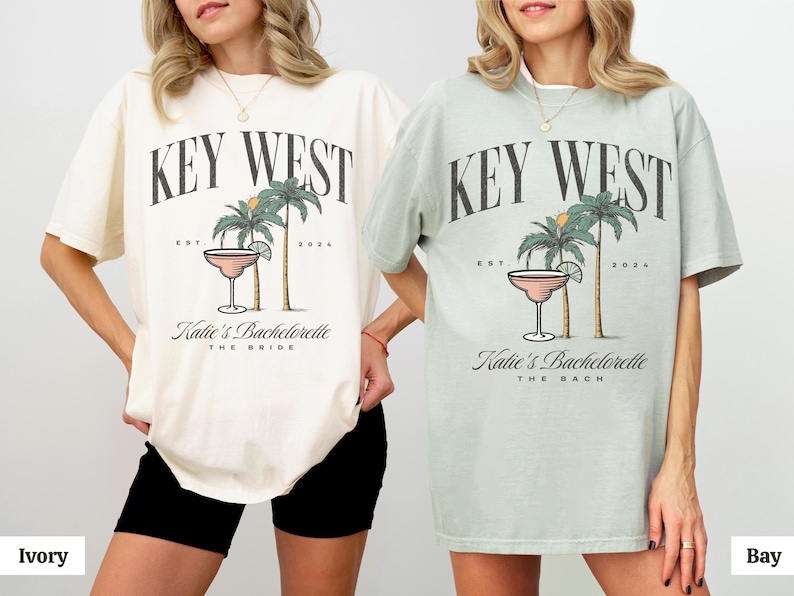 Peut inclure: Un t-shirt ivoire et un t-shirt vert baie, tous deux orn&eacute;s d'un imprim&eacute; graphique avec le texte KEY WEST, EST 2024, Katie's Bachelorette, et THE BRIDE ou THE BACH. Le motif inclut deux palmiers et un verre &agrave; cocktail avec un quartier de citron vert.