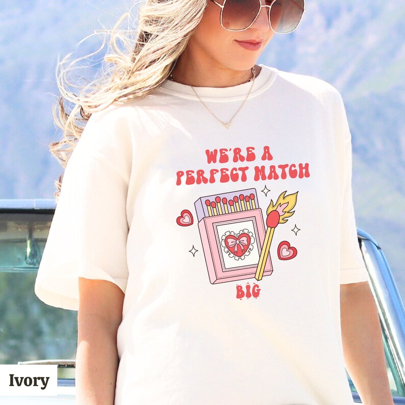 May include: White t-shirt with a graphic of a matchbox with the text "We're a perfect match" and "Big" printed on the shirt.