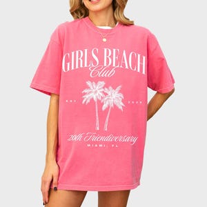 May include: Pink oversized t-shirt with a white graphic print of palm trees and the text "Girls Beach Club Est. 2020 20th Friendiversery Miami, FL"