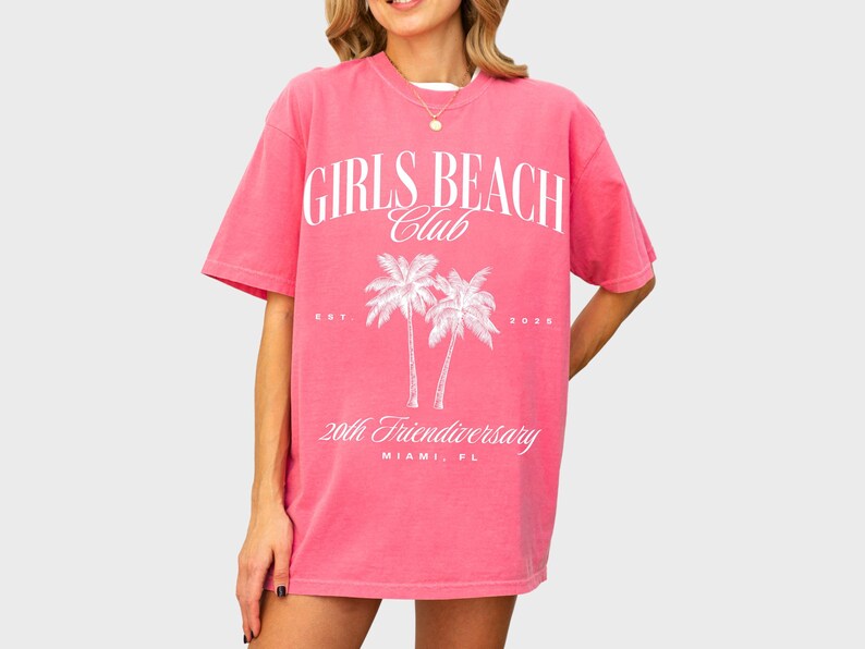 May include: Pink oversized t-shirt with a white graphic print of palm trees and the text "Girls Beach Club Est. 2020 20th Friendiversery Miami, FL"