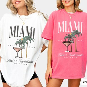Peut inclure: Un t-shirt blanc et un t-shirt rose, chacun arborant un imprim&eacute; graphique avec le texte MIAMI, EST 2024, Katie's Bachelorette, et THE BRIDE ou THE BACH, accompagn&eacute; d'illustrations de palmiers et d'un verre &agrave; cocktail avec un quartier de citron vert.