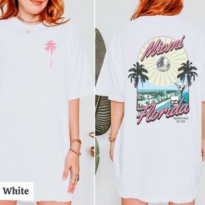 May include: White oversized t-shirt with a pink palm tree graphic on the front and a graphic on the back that says "Miami Florida" with a palm tree, a disco ball, and a martini glass. The text "Kirsten's Bach Est 2024" is below the graphic.