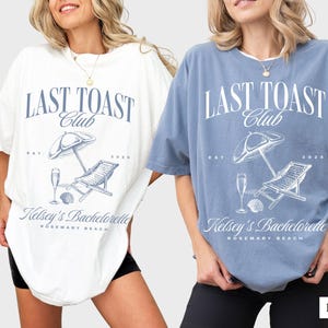 May include: Two women wearing oversized t-shirts with the text "LAST TOAST Club" and a beach scene graphic. The shirts are in white and blue jean colors. The text below the graphic says "Kelsey's Bachelorette Rosemary Beach".
