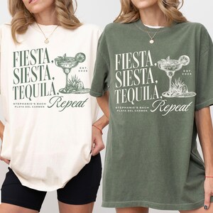 Puede incluir: Dos camisetas de gran tama&ntilde;o con un estampado gr&aacute;fico de una copa de margarita y el texto "Fiesta, Siesta, Tequila Repeat". La camiseta de la izquierda es de color marfil y la camiseta de la derecha es de color verde musgo.