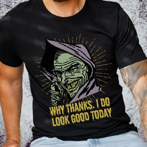 May include: Black t-shirt with a graphic of a green monster with gold teeth wearing a purple hooded robe. The text "Why thanks. I do look good today" is printed in yellow below the monster.