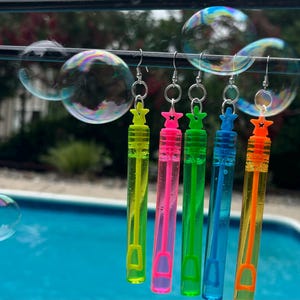May include: Five colorful bubble wands with star-shaped charms hanging from a wire. The wands are filled with different colored bubble solution and have a clear plastic tube.