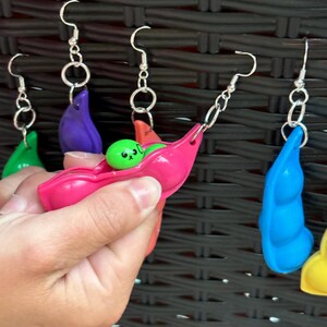 May include: Five pairs of earrings with a peapod design. Each earring features a different colored peapod with a small green pea inside. The peas have cute faces drawn on them.