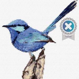 May include: A cross-stitch design of a blue bird with a long tail, perched on a branch. The bird is rendered in shades of blue, with a detailed, pixelated texture. A badge with the word "TESTED" is in the upper right corner.