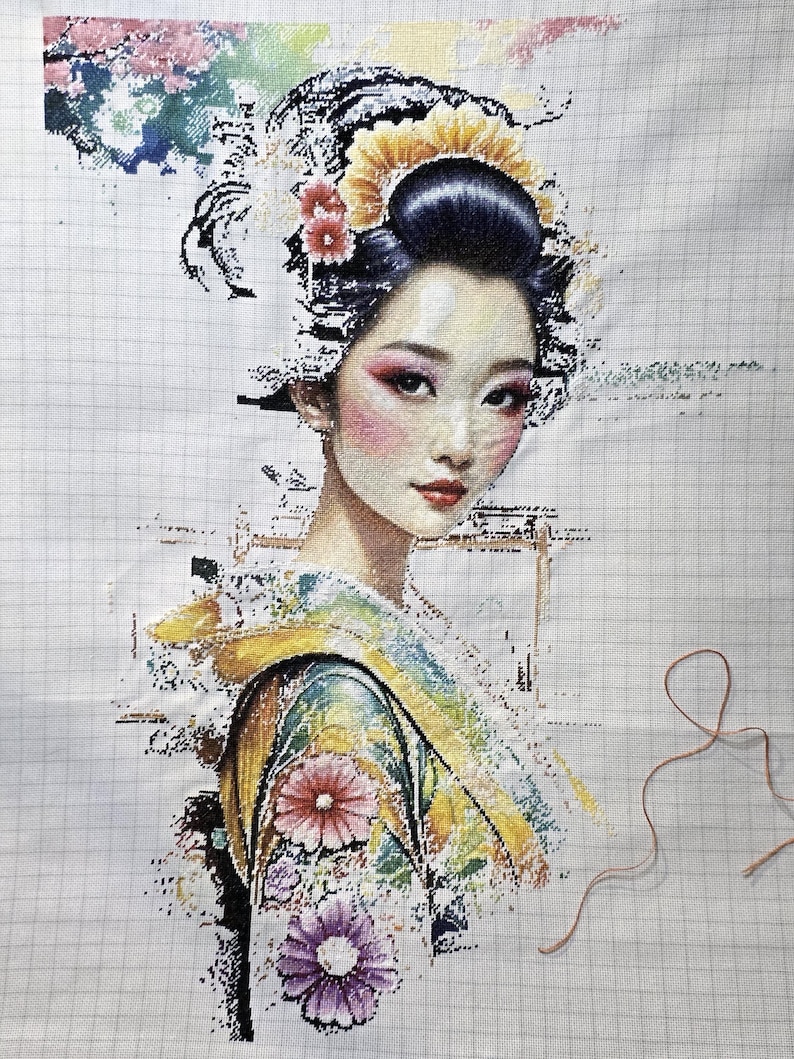 May include: A cross-stitch embroidery project on a white gridded fabric featuring a portrait of a person with dark hair styled in an updo adorned with yellow and red floral accents. The person wears a colorful patterned garment with pink and purple flowers.