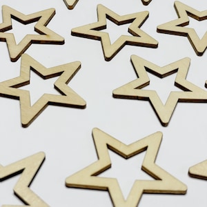 May include: A collection of ten unfinished wooden star shapes, each with a cutout in the center. The stars are arranged in a scattered pattern on a white background.