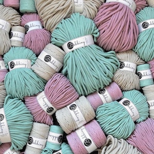 May include: A collection of Bobbiny brand cotton cord spools in various sizes and colors, including mint green, dusty pink, and beige. Each spool features a white paper label with the brand name Bobbiny printed in black text.