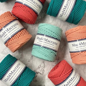 May include: An overhead shot displays several spools of Mad4Macrame cord in various colors, including coral, teal, and peach. Each spool is labeled with the brand name and product details. The cords are made of 100% cotton and are approximately 108 yards long.