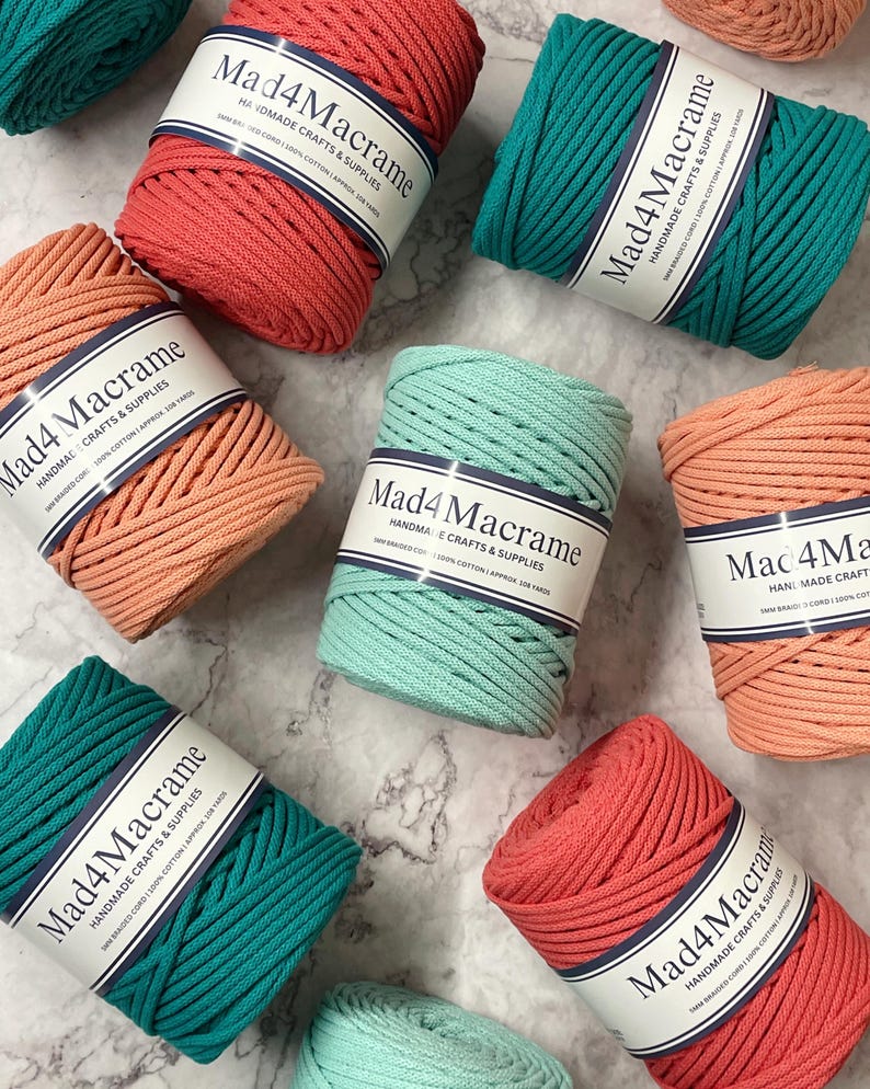 May include: An overhead shot displays several spools of Mad4Macrame cord in various colors, including coral, teal, and peach. Each spool is labeled with the brand name and product details. The cords are made of 100% cotton and are approximately 108 yards long.