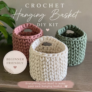 May include: Three crochet hanging baskets in pink, cream, and green. The baskets are cylindrical with a handle opening. Text on the image reads "CROCHET Hanging Basket DIY KIT" and "BEGINNER FRIENDLY". The bottom text says "Everything you need to make your own hanging basket".