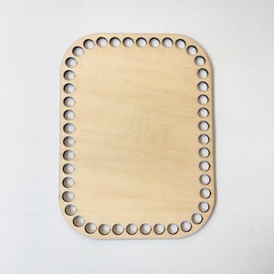 May include: A light-colored, rectangular wooden basket base with rounded corners. The perimeter features evenly spaced holes for weaving. The wood has a smooth, natural finish, ideal for crafting.