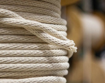 Puede incluir: Primer plano de un carrete de cuerda de algodón blanco natural. La cuerda está enrollada apretadamente y tiene una superficie ligeramente texturizada.