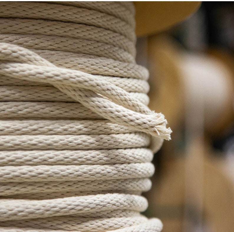 May include: Close-up of a reel of natural white cotton rope. The rope is tightly wound and has a slightly textured surface.