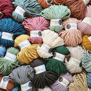 May include: A collection of multiple skeins of cotton cord in various colors, including blue, pink, green, yellow, brown, and cream. Each skein is secured with a white paper band featuring the brand name Bobbiny printed in black text.
