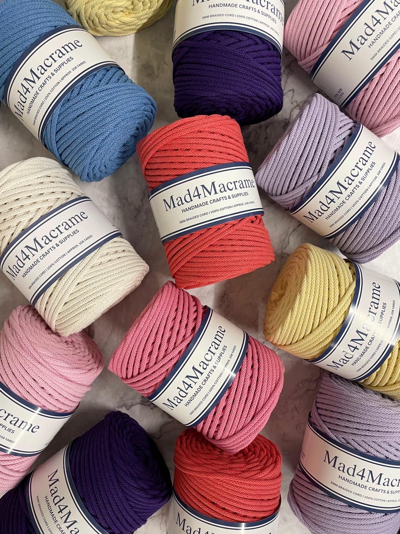 May include: An overhead shot of several spools of Mad4Macrame brand braided cord in various colors, including blue, pink, red, purple, yellow, and cream. Each spool is labeled with the brand name and product details.