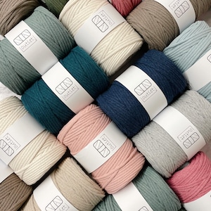 May include: An overhead shot of several spools of yarn in various colors, including teal, navy, pink, and beige. Each spool is wrapped with a white label that reads "outlet". The yarn is tightly wound and appears to be made of a soft, natural fiber.