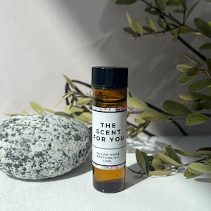May include: A small brown glass bottle with a black cap and a white label that says "THE SCENT FOR YOU" and "TAILOR-MADE PERFUME/OIL 10ML".