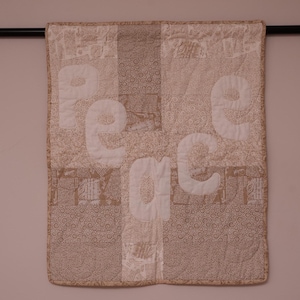 Puede incluir: Una pared acolchada beige con la palabra "paz" escrita en letras de tela blanca.