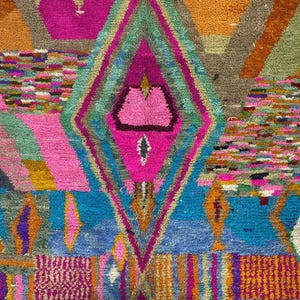 The image is a vibrant and colorful abstract rug with a diamond-shaped motif at its center. The rug features a variety of geometric shapes, patterns, and colors, creating a visually striking and dynamic composition.