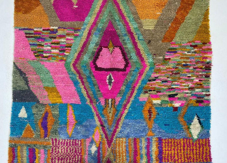 The image is a vibrant and colorful abstract rug with a diamond-shaped motif at its center. The rug features a variety of geometric shapes, patterns, and colors, creating a visually striking and dynamic composition.