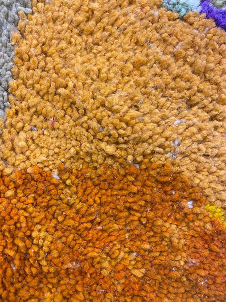 The image is a close-up of a textured surface with a mix of orange, yellow, and gray colors. The surface appears to be a carpet or rug with a variety of textures and patterns.