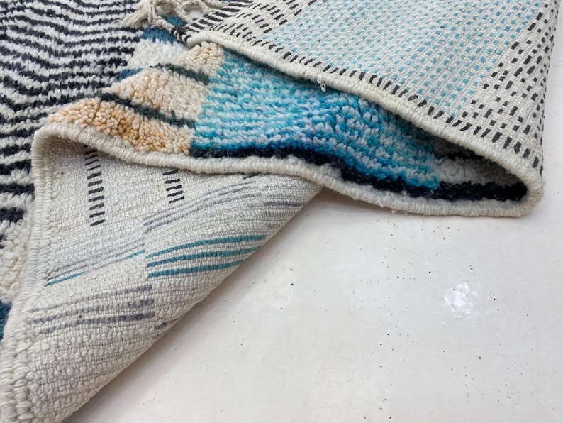 a close-up view of a colorful rug with a geometric pattern, featuring a mix of blue, white, and black colors.