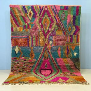 a vibrant, colorful rug with a geometric pattern and a variety of shapes and colors, including shades of pink, green, blue, and orange.