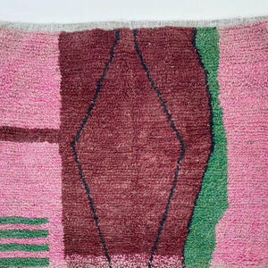 a vibrant, multicolored rug with a geometric pattern. The rug has a mix of pink, green, and brown colors, creating a visually striking and eye-catching design.