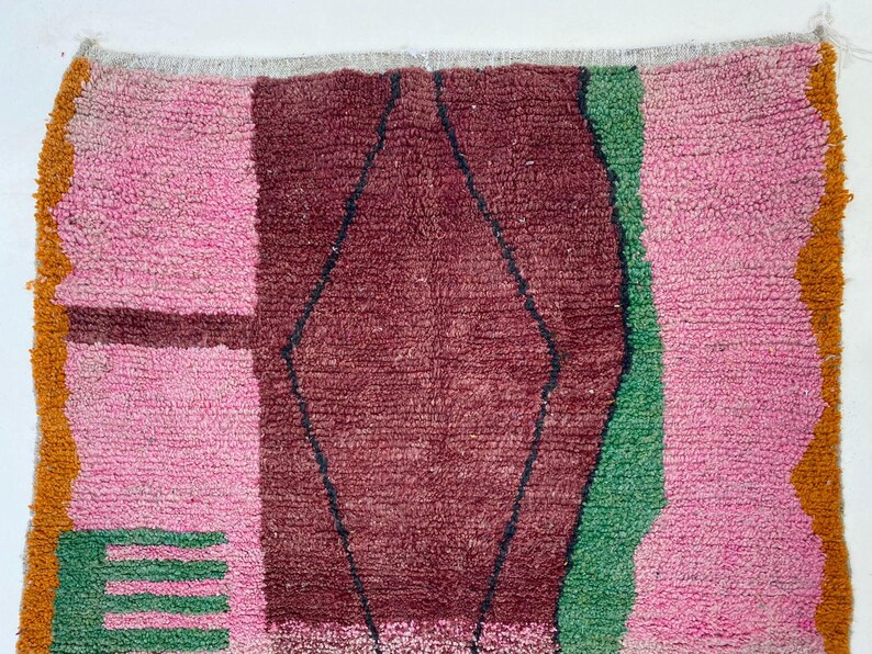 a vibrant, multicolored rug with a geometric pattern. The rug has a mix of pink, green, and brown colors, creating a visually striking and eye-catching design.