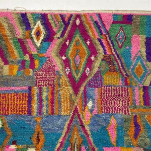 The image is a vibrant and colorful rug with a geometric pattern of various shapes and colors, including diamonds, triangles, and squares. The rug appears to be a traditional or handmade textile, with a rich and intricate design that showcases the craftsmanship and artistry of the creator.