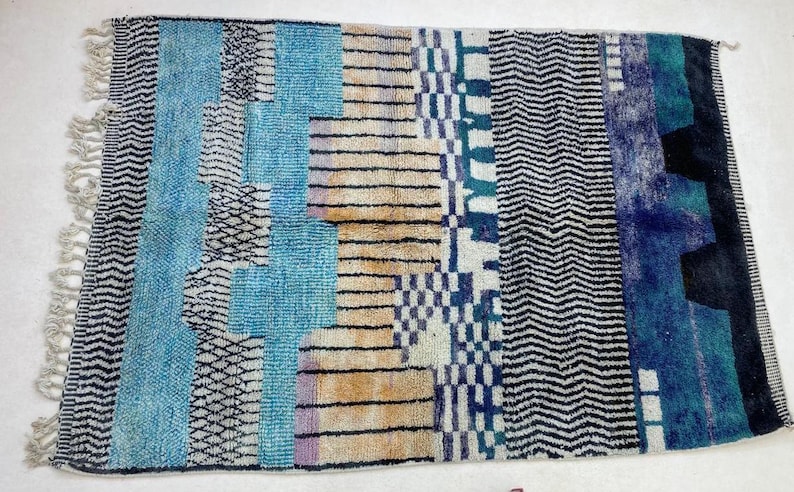 a vibrant, multicolored rug with a geometric pattern of stripes, zigzags, and geometric shapes in various shades of blue, black, and white.