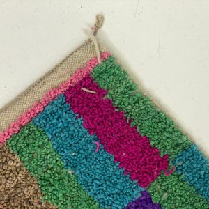 A colorful, multicolored rug with a geometric pattern of stripes in various shades of pink, blue, green, and purple.