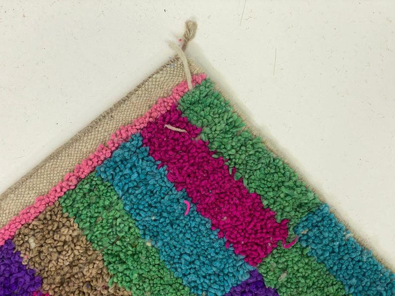A colorful, multicolored rug with a geometric pattern of stripes in various shades of pink, blue, green, and purple.