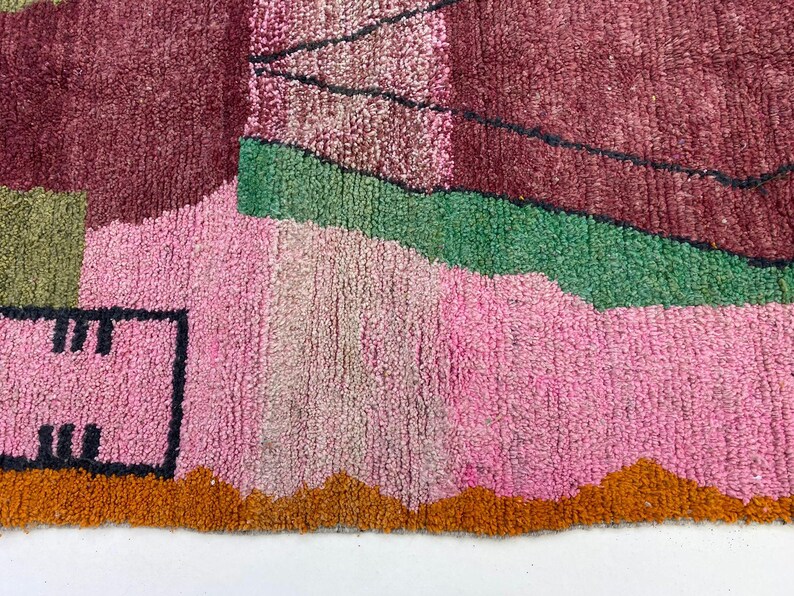 The image is a close-up of a colorful, abstract rug with various shades of pink, green, and orange.