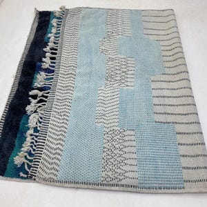a colorful, patterned rug with a mix of blue, gray, and black colors. The rug has a textured design with various geometric shapes and patterns, creating a visually interesting and vibrant piece.