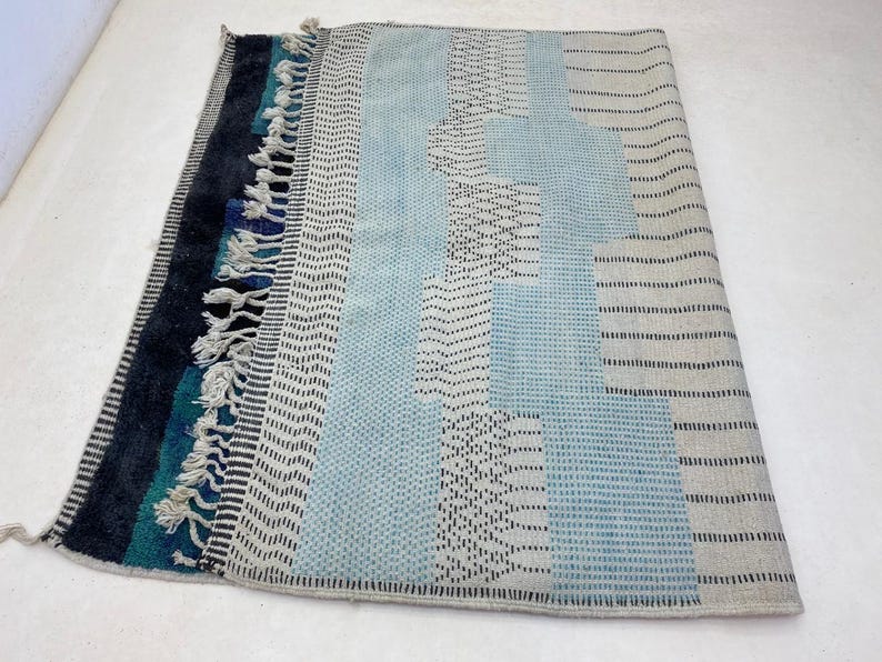 a colorful, patterned rug with a mix of blue, gray, and black colors. The rug has a textured design with various geometric shapes and patterns, creating a visually interesting and vibrant piece.