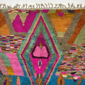 The image is a vibrant and colorful rug with a geometric pattern, featuring a variety of shapes and colors such as pink, green, blue, and orange.