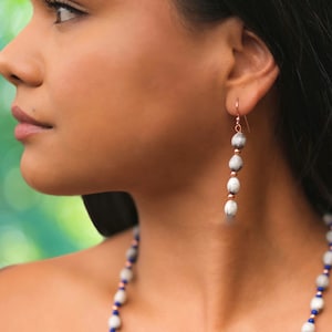 May include: A pair of dangle earrings with white and gray beads and rose gold accents.