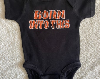 May include: Black baby onesie with orange and black tiger stripes that says "BORN INTO THIS" in white letters.