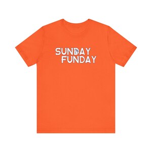 Pu&ograve; includere: T-shirt arancione brillante con la scritta "SUNDAY FUNDAY" in lettere bianche. La maglietta &egrave; a girocollo e sembra essere realizzata in un materiale morbido e confortevole. Il testo ha un'atmosfera giocosa e informale.