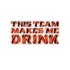 May include: A sticker with an orange and black tiger stripe pattern that says "This team makes me drink".