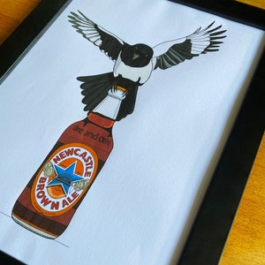 May include: A black and white magpie perched on top of a brown glass bottle with a white label that reads "Newcastle Brown Ale" and "One and Only".