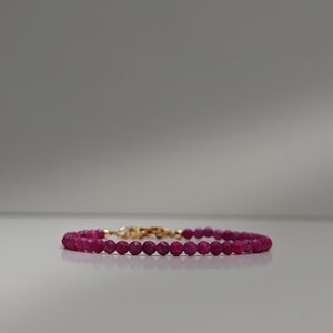 May include: A delicate bracelet featuring small, faceted, deep pink gemstones strung together. The bracelet is secured with a gold-coloured clasp. The gemstones are evenly sized and arranged, creating a continuous loop of colour.